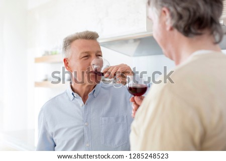 Mature men drinking wine while standing at home