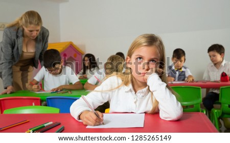 Portrait of bored schoolgirl sitting in classroom with classmates and teacher