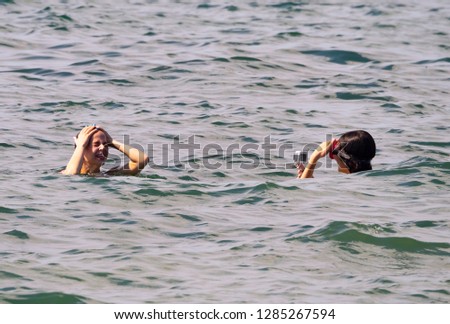 Girl holding action camera in waterproof case. Two sisters shoot a video on the sea coast. Compact gadget waterproof, support 4k video, voice controls and is often used in extreme photography