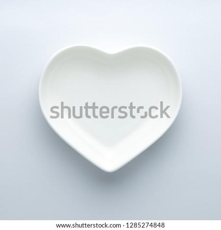 Empty plate in the shape of a heart on a white background in the center of the frame. Minimalism. Copy space. Modern ceramic glossy dishes. Concept of Valentine's Day or wedding romantic theme. Square