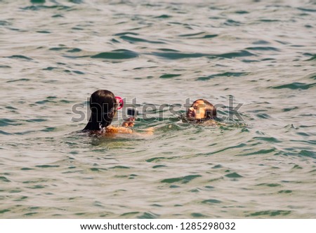 Girl holding action camera in waterproof case. Two sisters shoot a video on the sea coast. Compact gadget waterproof, support 4k video, voice controls and is often used in extreme photography