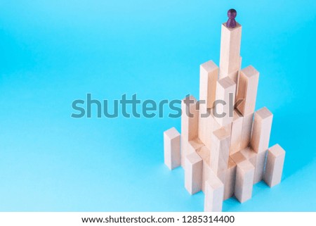 Abstract construction from wooden blocks with copy space on blue background. Business metaphor, abstract person on top of a career. The concept of success, achievement, victory.