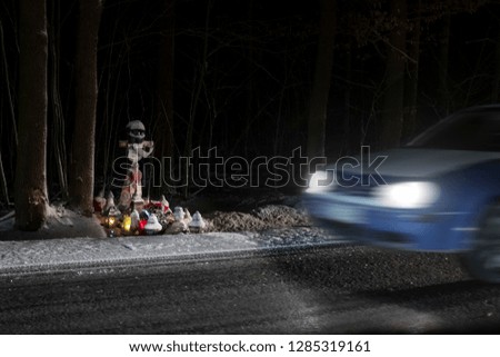 The cross of a motorcyclist on roadside and passing car at night