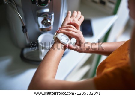 Top view close up picture of girl touching her white wristwatch. Coffee machine with cup on blurred background