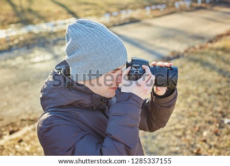 Young photographer in a hat, makes a photo on his camera in the winter park