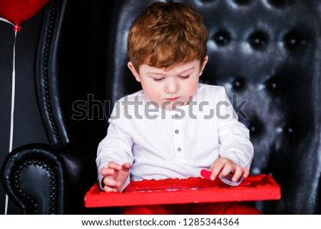 Little boy sitting on the armchair with red framed picture on the St. Valentine's day. Black background and mother's woman day concept.