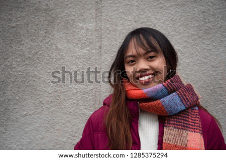 20s smile Filipino young teen woman Asian portrait with red coat and scarf with grey wall background 