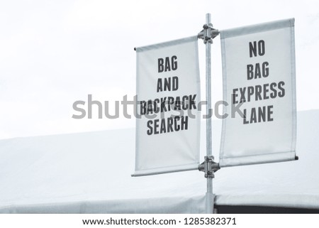 Security screening station outside of a venue entrance, with banners for "Bag and Backpack Search", and "No Bag Express Lane"