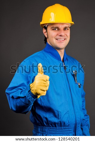 Young construction worker giving thumb up sign against gray