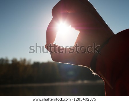 Hands catch sun at sunset time. Female fingers hold sun above lake level. 