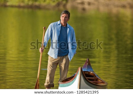 Portrait of a middle aged man standing with his canoe lakeside.