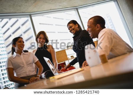 Four young business colleagues laughing while standing inside an office.