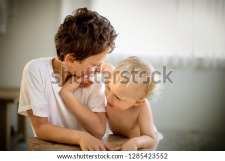 Young boy looking down at his younger brother while in a room inside their house.