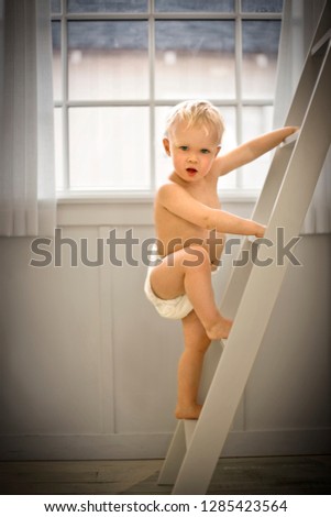 Portrait of a young toddler climbing a wooden ladder while only wearing nappies inside his home.