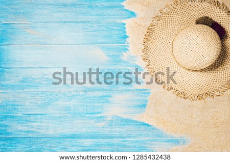 Top view of sandy beach with blue marine planks frame and summer accessories. Background with copy space and visible sand and wood texture. Border composition