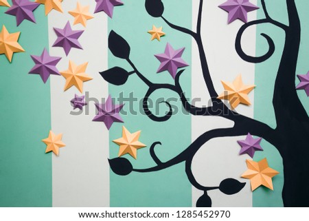 Close-up image of black tree with leaves, yellow and purple six-pointed stars on striped white and turquoise background in apartment. Family tree concept, genealogy, career growth, success metaphor