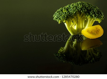 A sprig of broccoli with a slice of yellow cherry tomato isolated on a dark background with reflection.
