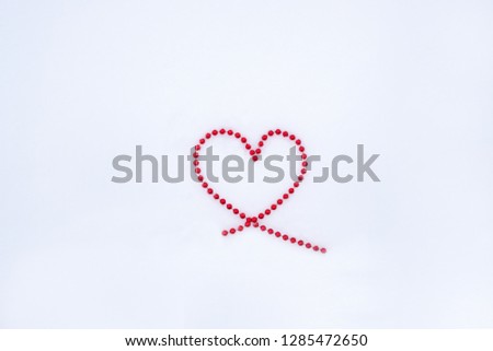 A heart laid out of beads on a background of white snow with space for text. Top view.