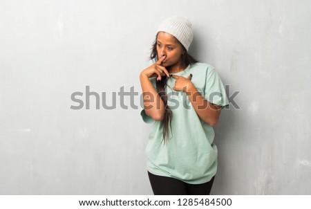 Young afro american woman on textured background showing a sign of silence gesture putting finger in mouth
