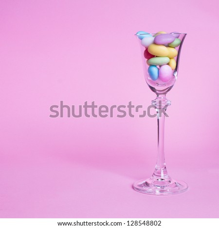 Colorful sweets in the bowl. A glass bowl with fanny colorful balls in it on the pink background.