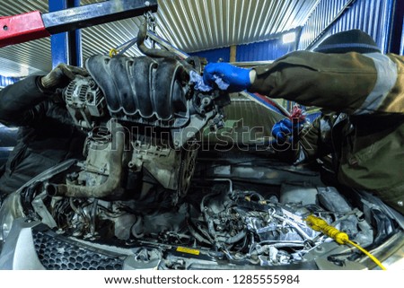 Close-up of the installation of the motor on an old car using a pneumatic manual crane in the auto repair shop. The work of auto mechanics to remove the engine