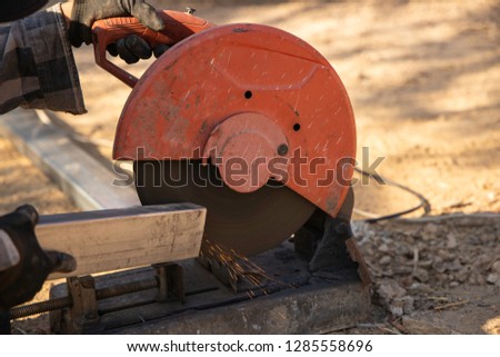 Mechanic using cut-off saw machine cutting steel bar with bright sparks in construction site