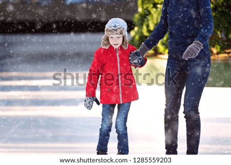 family of two, mother and son, enjoying ice skating together at outdoor skating rink at beautiful snowy day, family fun activity concept