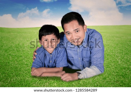 Picture of happy little boy hugged by his father while lying together in the meadow
