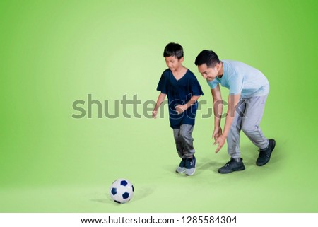 Picture of young man and his son playing football in the studio with green screen