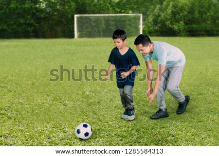 Picture of young man looks happy while playing football with his son in the soccer field
