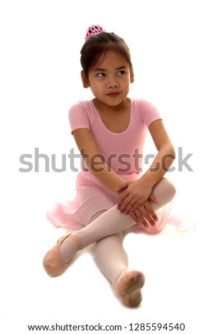Young girl in ballet dress sits posing on a white background
