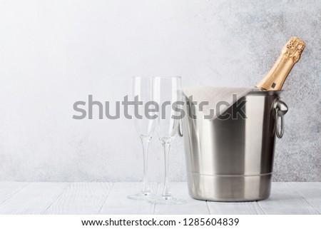 Champagne bottle in bucket and glasses in front of stone wall. With space for your text