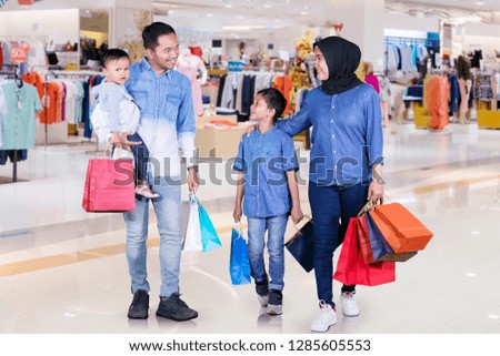 Picture of a happy Muslim family holding shopping bags while walking together in the mall