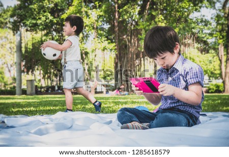 Little Young asian child boy playing online games on tablet computer and smart phone in nature park outdoors ,People lifestyle concept.
