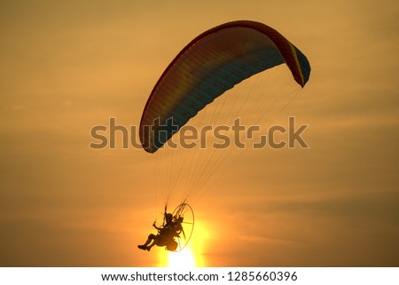 Silhouette picture of the Paramotors flying through sunlight sunset sky background.