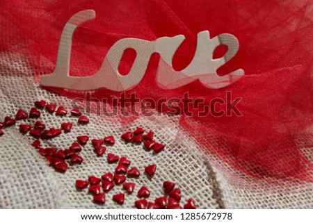 Love letters and hearts on beautiful red fabric background. The decoration of inscription love in translucent fabric looks like in red waves. Photo Pictures for postcards for Valentine’s day. 