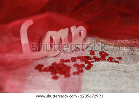 Love letters and hearts on beautiful red fabric background. The decoration of inscription love in translucent fabric looks like in red waves. Photo Pictures for postcards for Valentine’s day. 