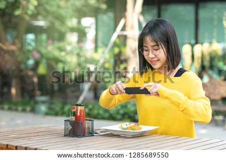 Young asian woman food blogger , vlogger or micro influencer taking photos for food blog using smartphone social network, sharing, food blogger concept. Young student yellow clothes is happy lunch.