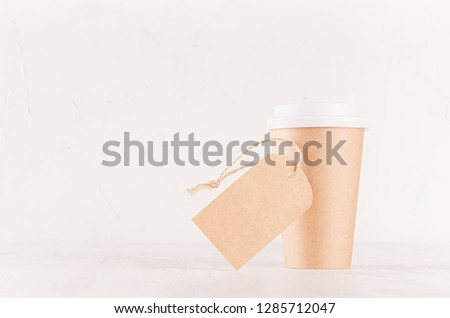 Coffee packing mockup -  craft brown paper cup with white cap and blank label on white wood board with copy space, coffee shop interior. 