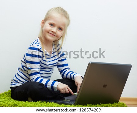 Smiling kid girl using laptop , seating on floor .