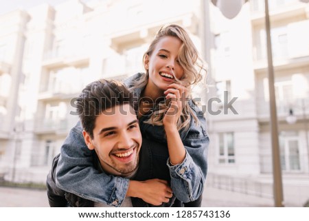 Blissful white man holding his girlfriend on city background. Relaxed romantic couple enjoying weekend walk.