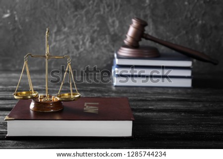 Scales of justice and book with title LAW on wooden table