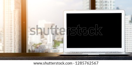 Computer,laptop with blank screen on wood table with office window view backgrounds.  Using for Mock up template for craft display of your design,Banner for advertise of product.