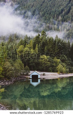 Boat house reflected in a calm lake in the North Cascades National Park with morning mist