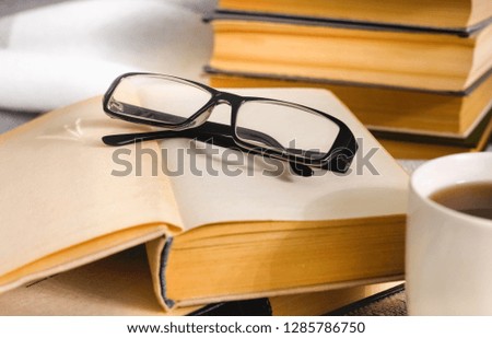 Stack of open vintage books with glasses and  cup of tea on  table