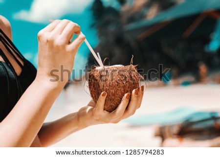 Close up of girl drinking cocktail in coconut while standing on the beach.