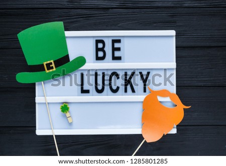 Lightbox with title Be lucky and photobooth green hat and and orange beard on wooden sticks. Creative background to St. Patricks Day