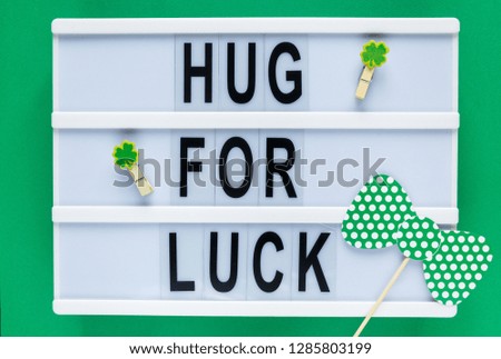 Lightbox with title Hug for luck and photobooth green bow tie on wooden sticks on green background. Creative background to St. Patricks Day