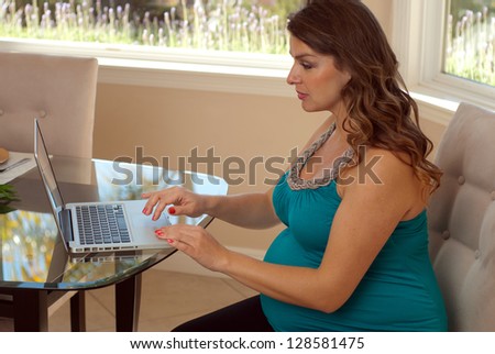 Pregnancy and technology - Pregnant woman using laptop computer at home.
