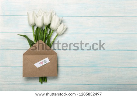 A bouquet of white tulips with a love note and envelope on blue wooden boards. Top view with place for your congratulations.